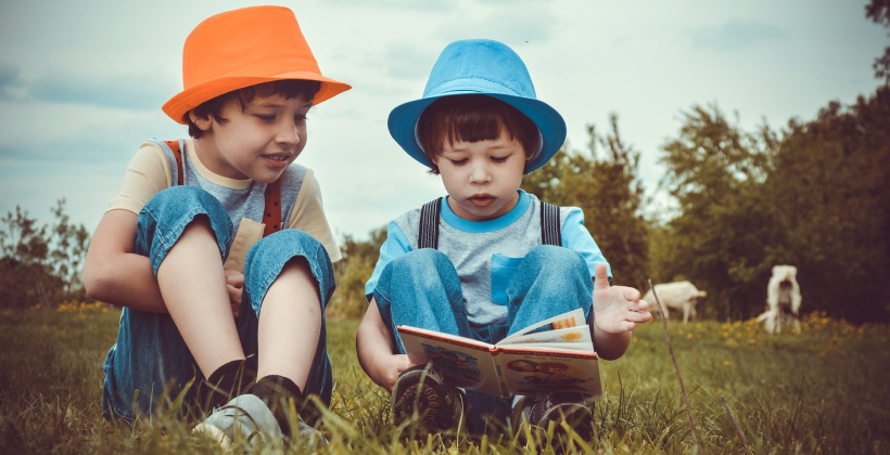 Zwei Kinder lesen auf einer Wiese.